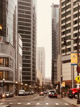 View of city street amidst tall skyscrapers on an overcast day, featuring urban architecture.