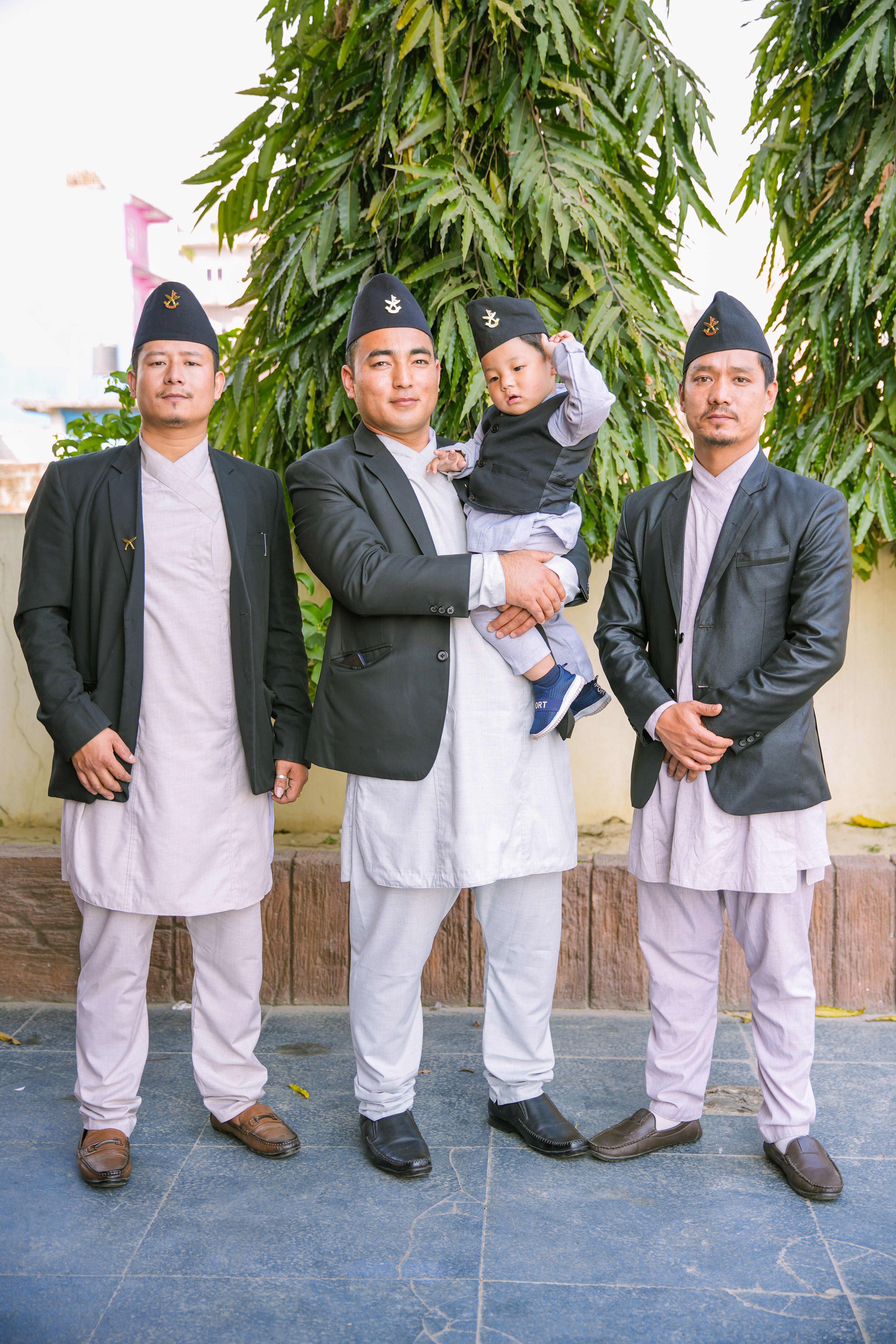 A group of Nepali men and a baby wearing traditional attire posing outdoors.