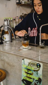 A young woman barista skillfully prepares a coffee drink in a cozy cafe in Madiun, Indonesia.