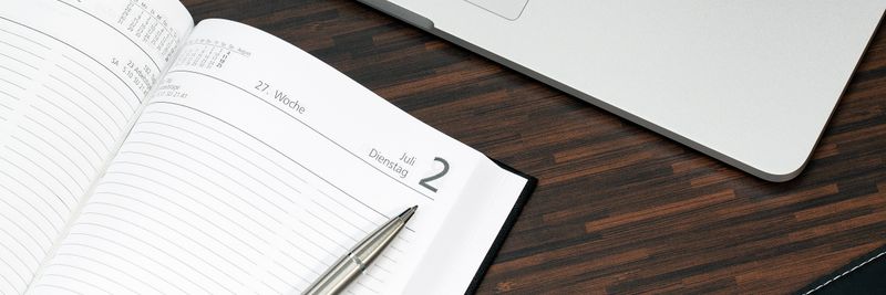 Open planner with a pen and laptop on a wooden desk, ready for organization.
