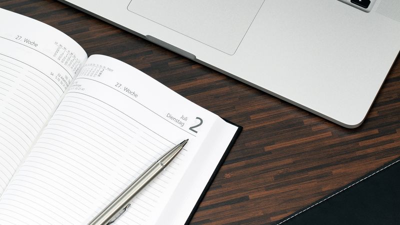 Open planner with a pen and laptop on a wooden desk, ready for organization.