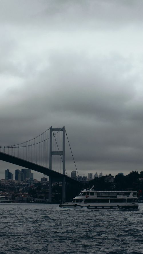 Free Fatih Sultan Mehmet Bridge with a boat cruising under cloudy skies in Istanbul, Turkey. Stock Photo