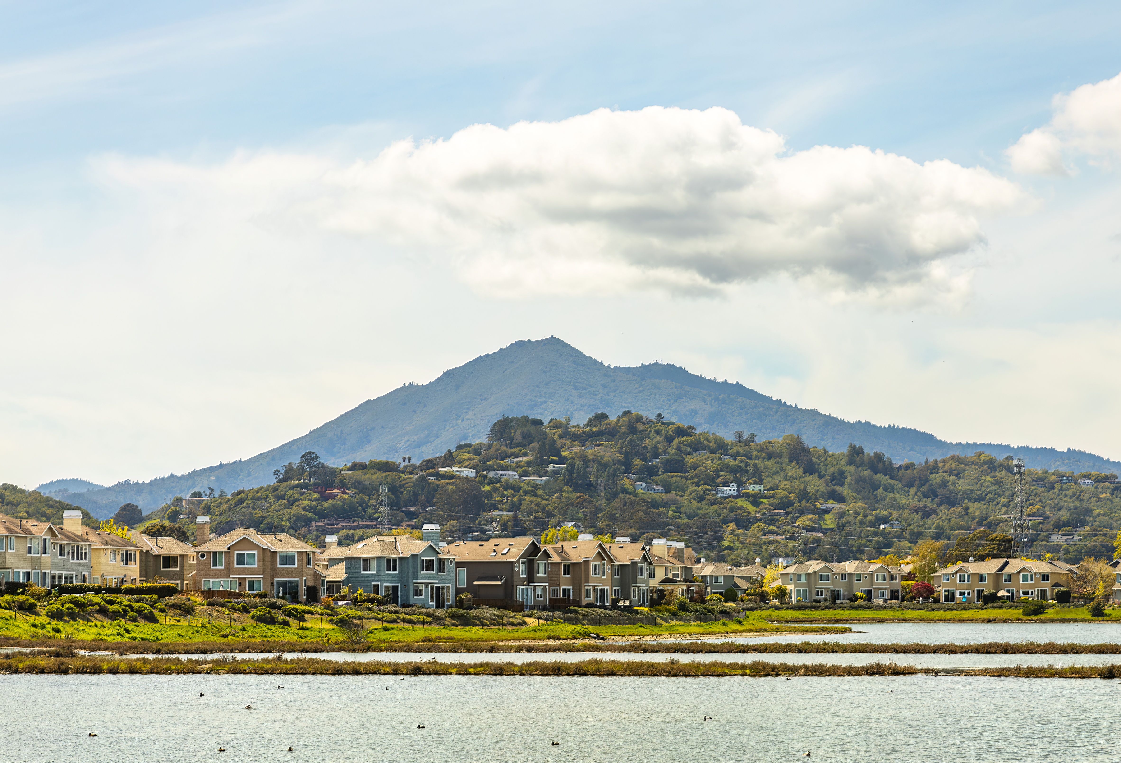 Scenic view of waterfront houses against a stunning mountain backdrop under a clear sky.