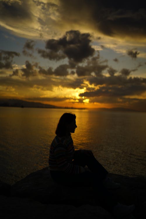 Silhouette of Sitting Woman on Sea Shore at Sunset