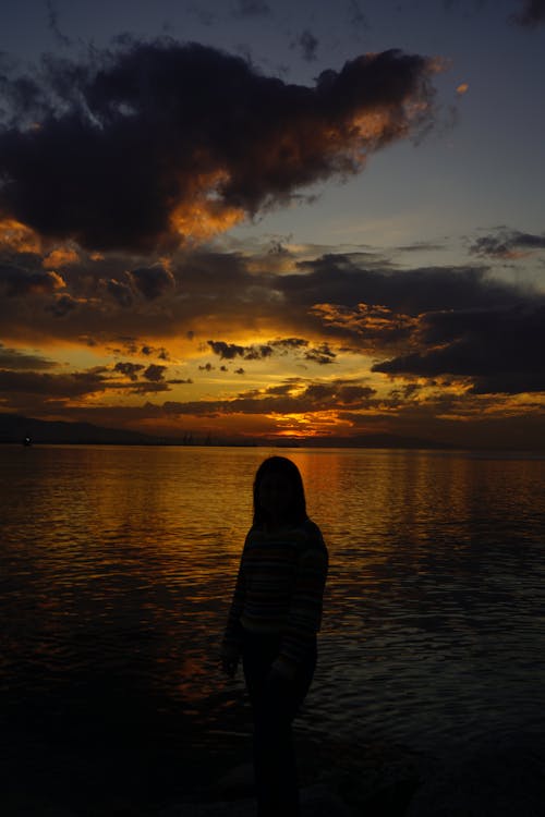 Silhouette of Woman Standing on Sea Shore at Sunset