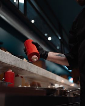 A chef wearing black gloves handles a ketchup bottle in an Istanbul kitchen.