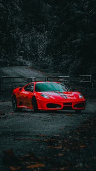 Vivid red sports car parked on a serene forest path, creating a moody and dramatic scene.