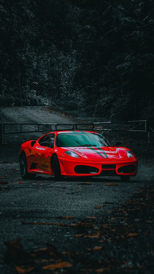 Free Vivid red sports car parked on a serene forest path, creating a moody and dramatic scene. Stock Photo