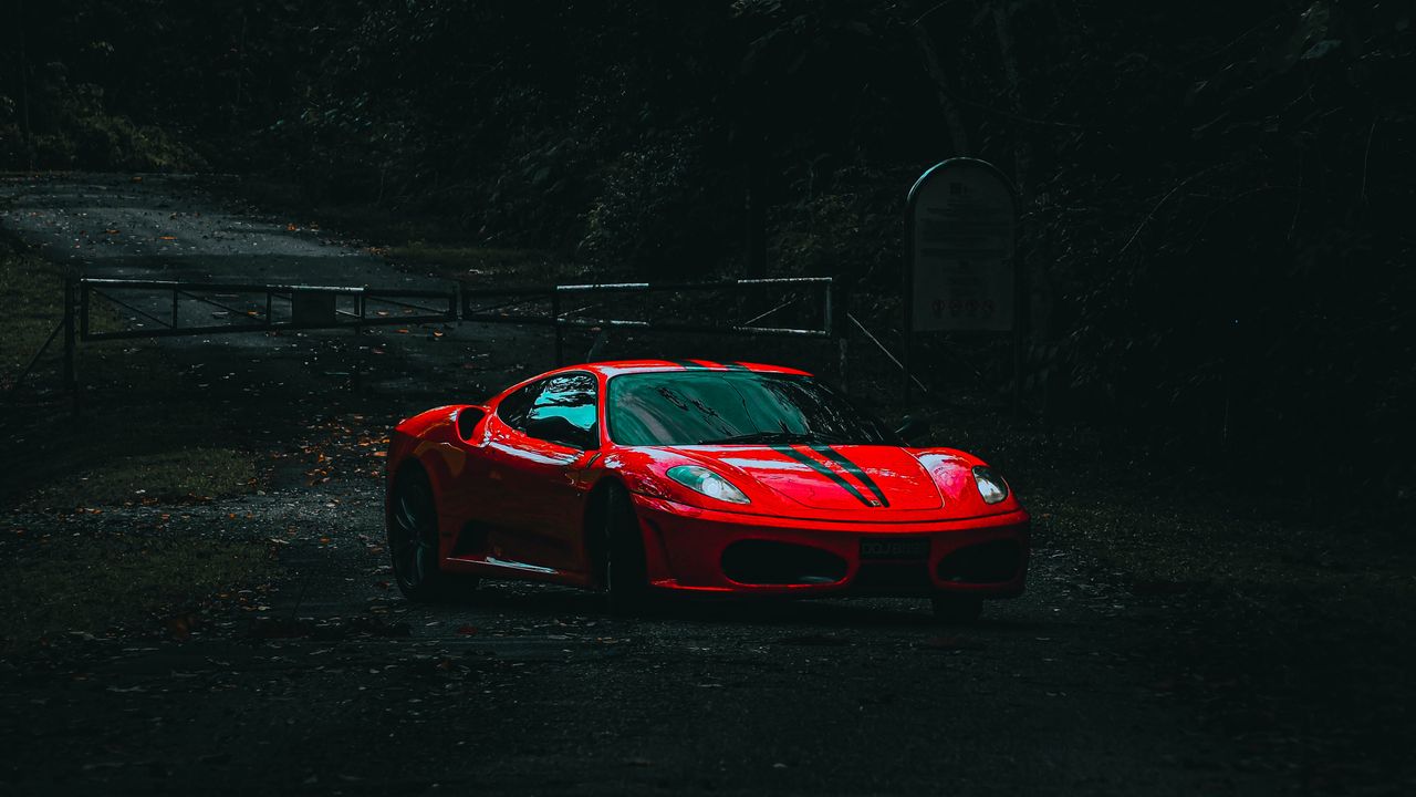 dramatic shot of a red sports car on a secluded dark forest road