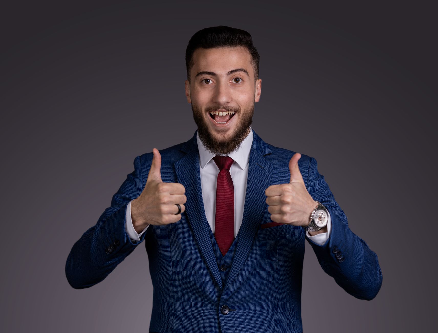A smiling businessman in a blue suit gives a thumbs up, portraying success and confidence.