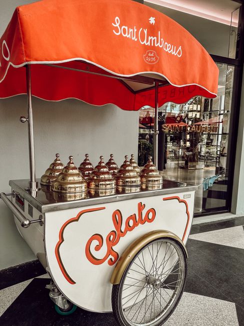 Retro gelato cart with metal lids and red canopy outside a small business.