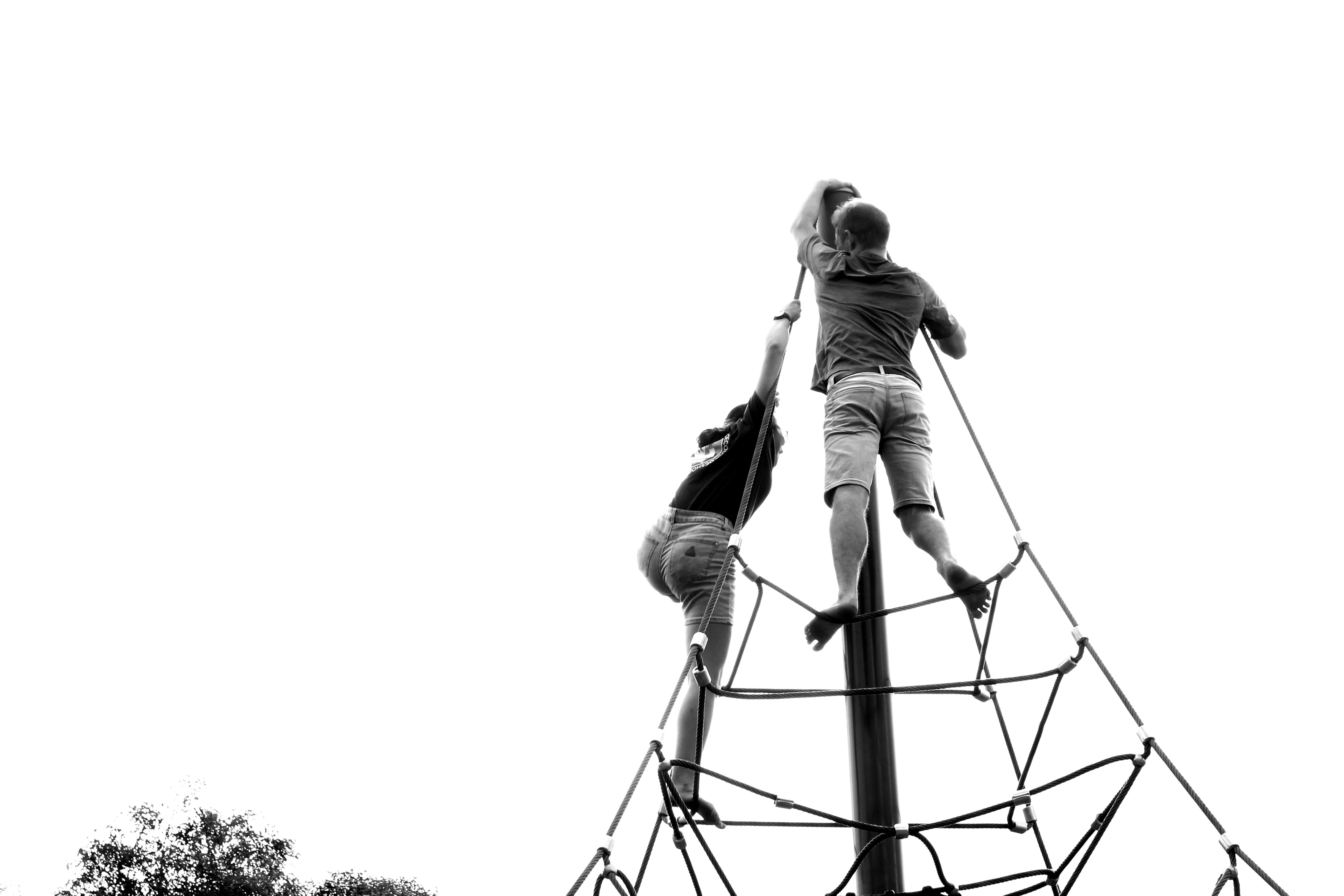 Two people climbing a playground rope structure in a black and white setting.
