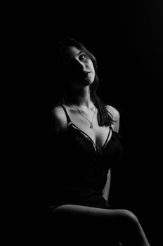 Artistic black and white studio portrait of a young woman in lingerie, creating a sensual silhouette.