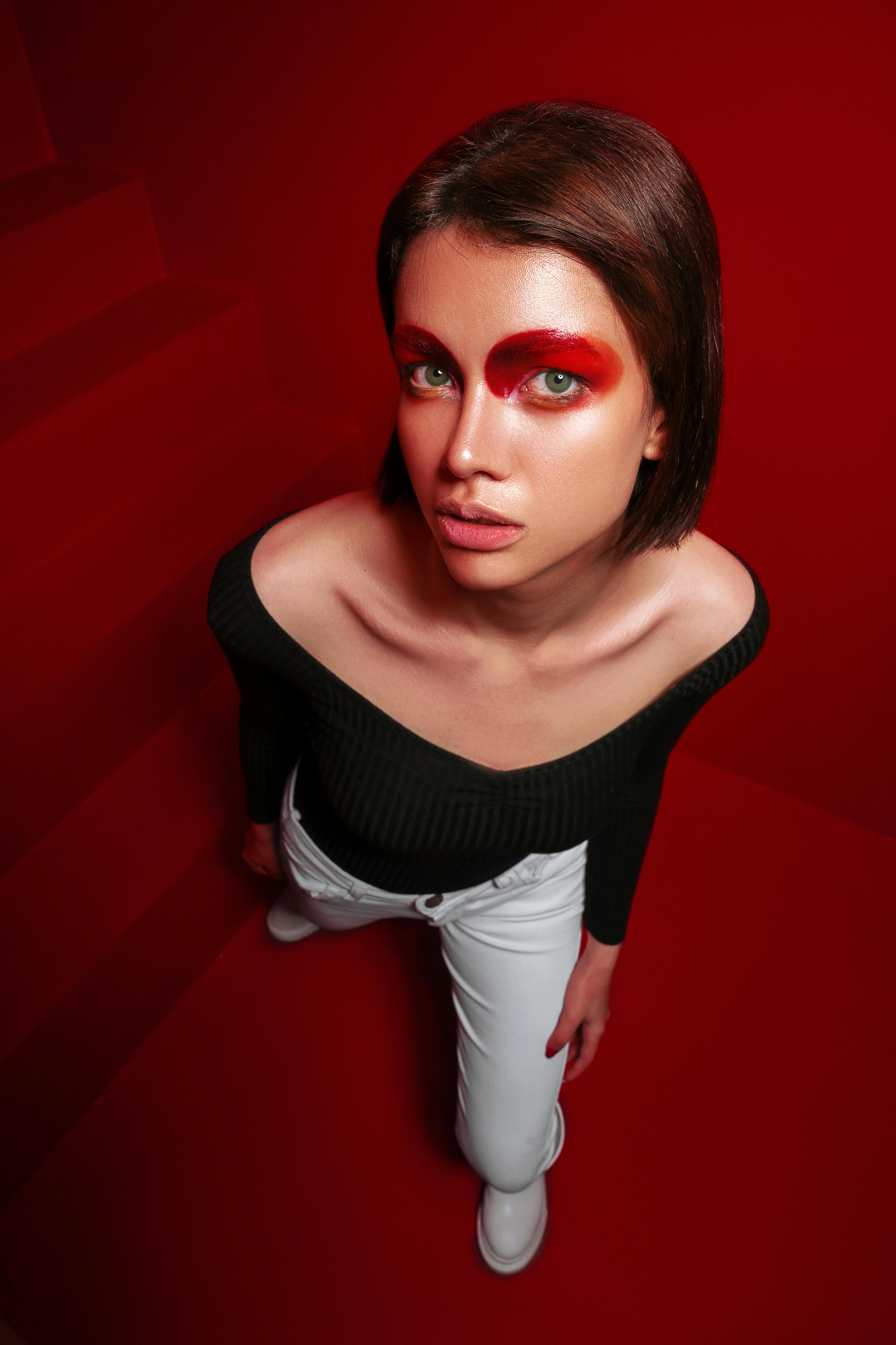 Young woman with striking red eye makeup standing against a vivid red background. Stylish high angle shot.