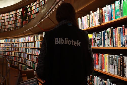 Librarian in Jacket Standing by Bookshelves