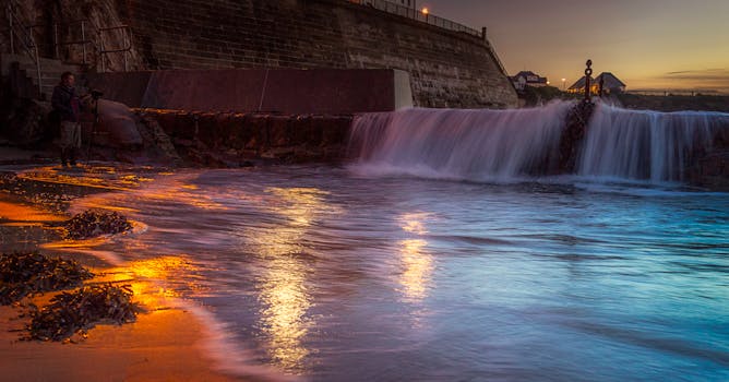 日落时分，摄影师捕捉到一个宁静的瀑布流入大海并倒映着晚霞的时刻