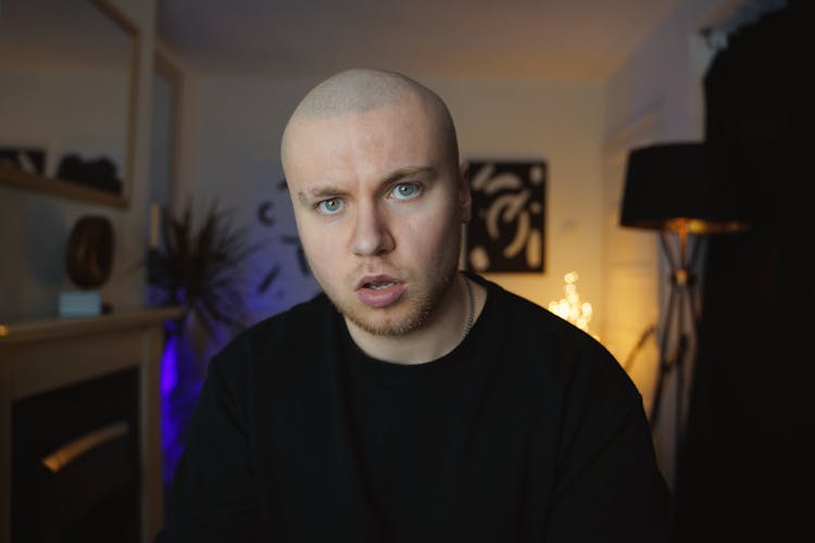 A Young Bald Man Sitting In A Room 