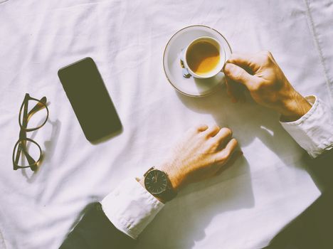 Flat lay of man enjoying espresso with smartphone, watch, and glasses on a table.