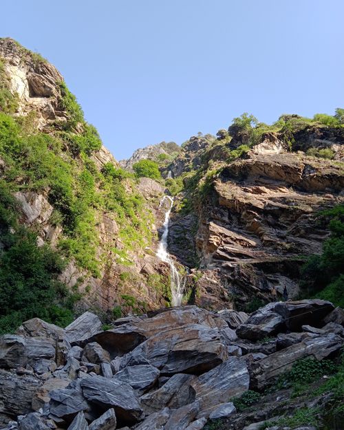 Free Beautiful waterfall cascading through a rocky canyon on a sunny day, surrounded by lush greenery in Delhi, India. Stock Photo