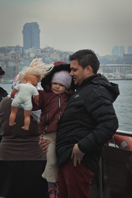 Free Father holding child with doll by the waterfront, urban skyline in the background. Stock Photo
