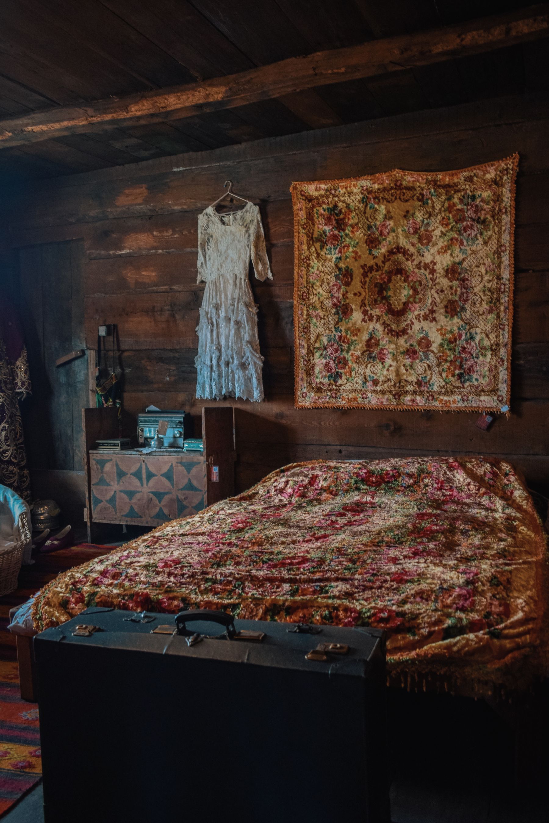 Warm traditional bedroom with a colorful quilt, wooden furniture, floral decoration and an old suitcase
