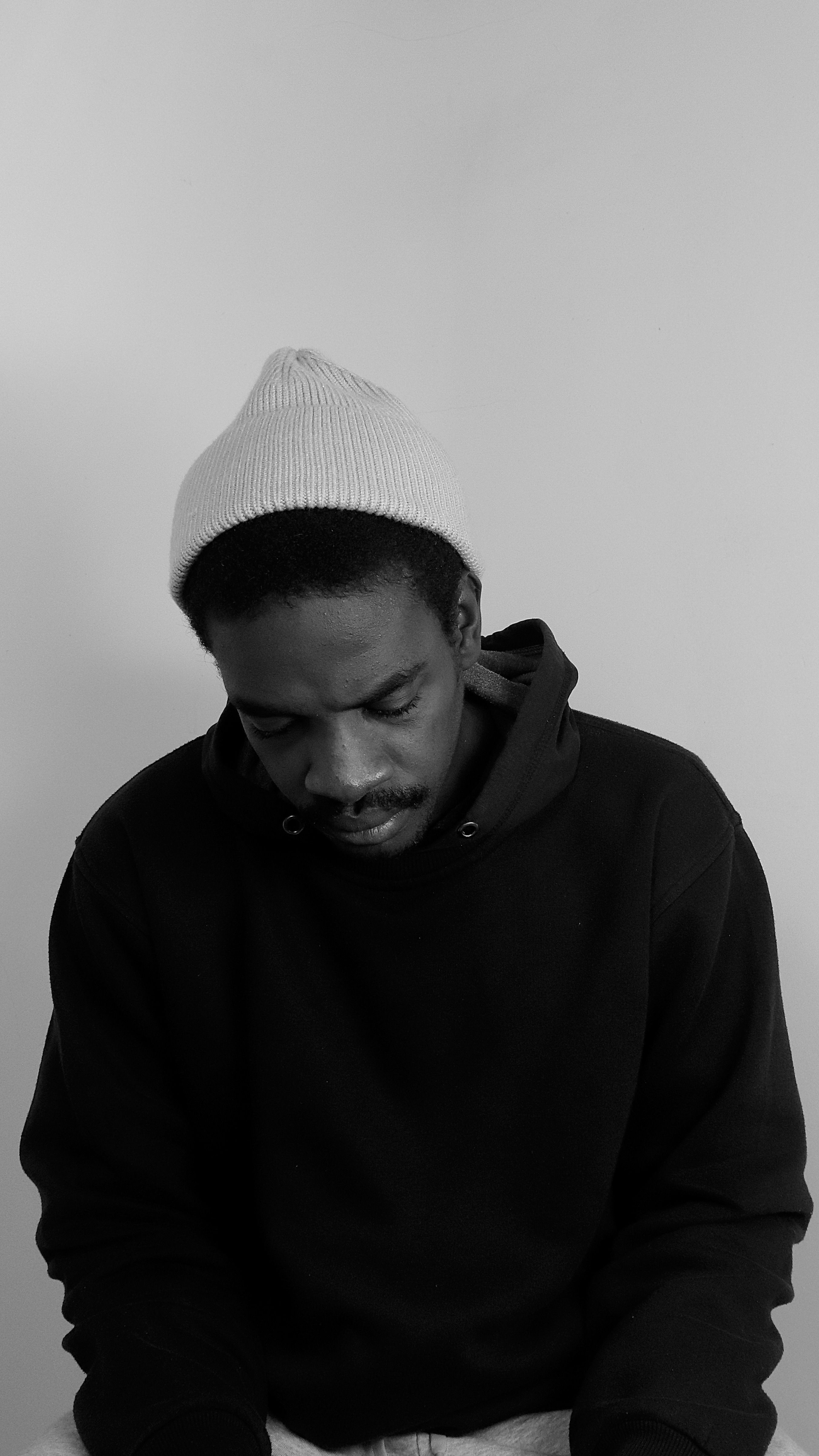 Monochrome portrait of a man wearing a beanie, looking down, in a studio shot.