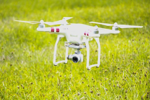 White quadcopter drone flying over a bright green grass field. Captured in clear daylight outdoors.