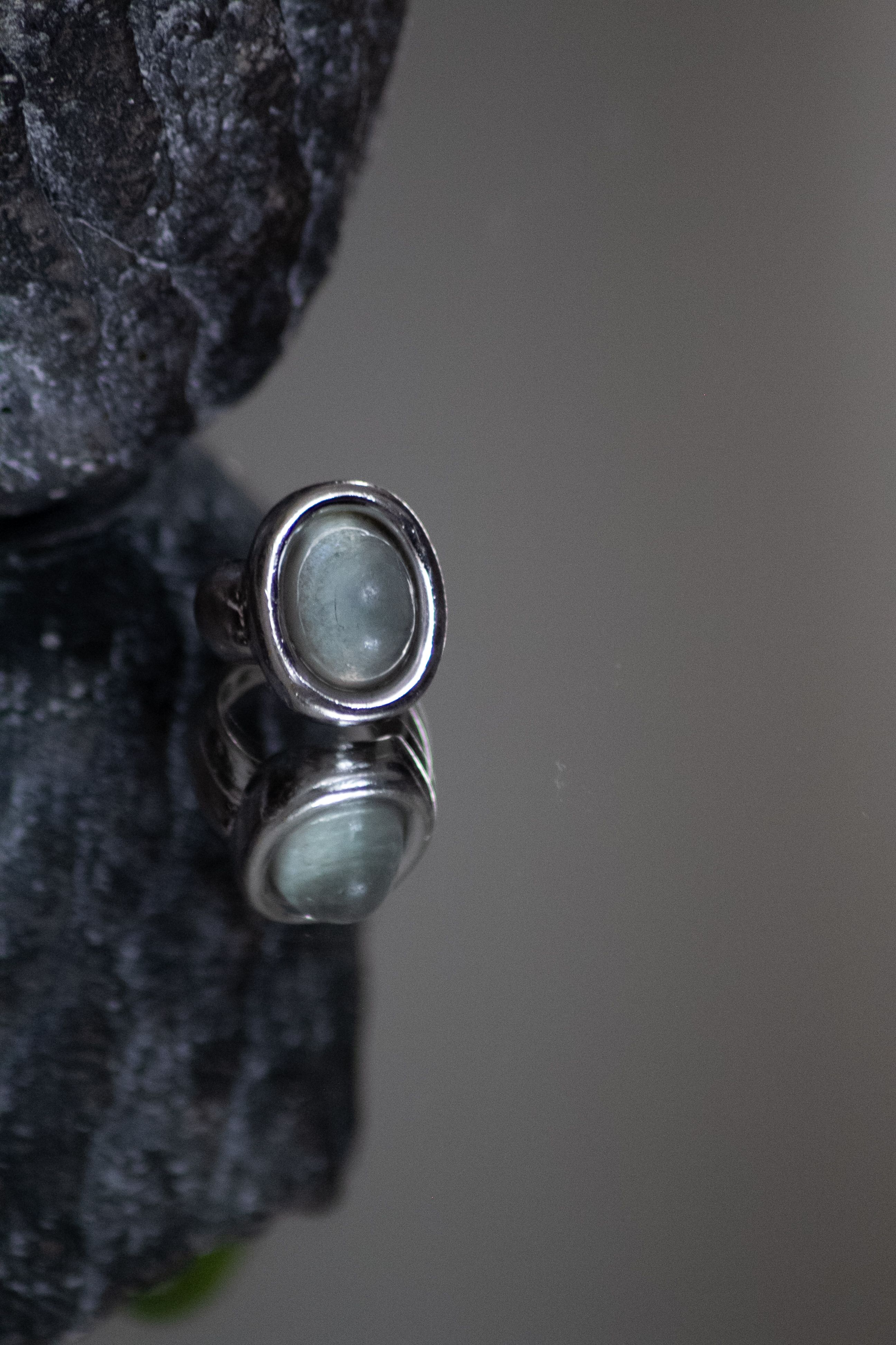 Close-up image of a silver ring with a gemstone, reflecting on a surface.