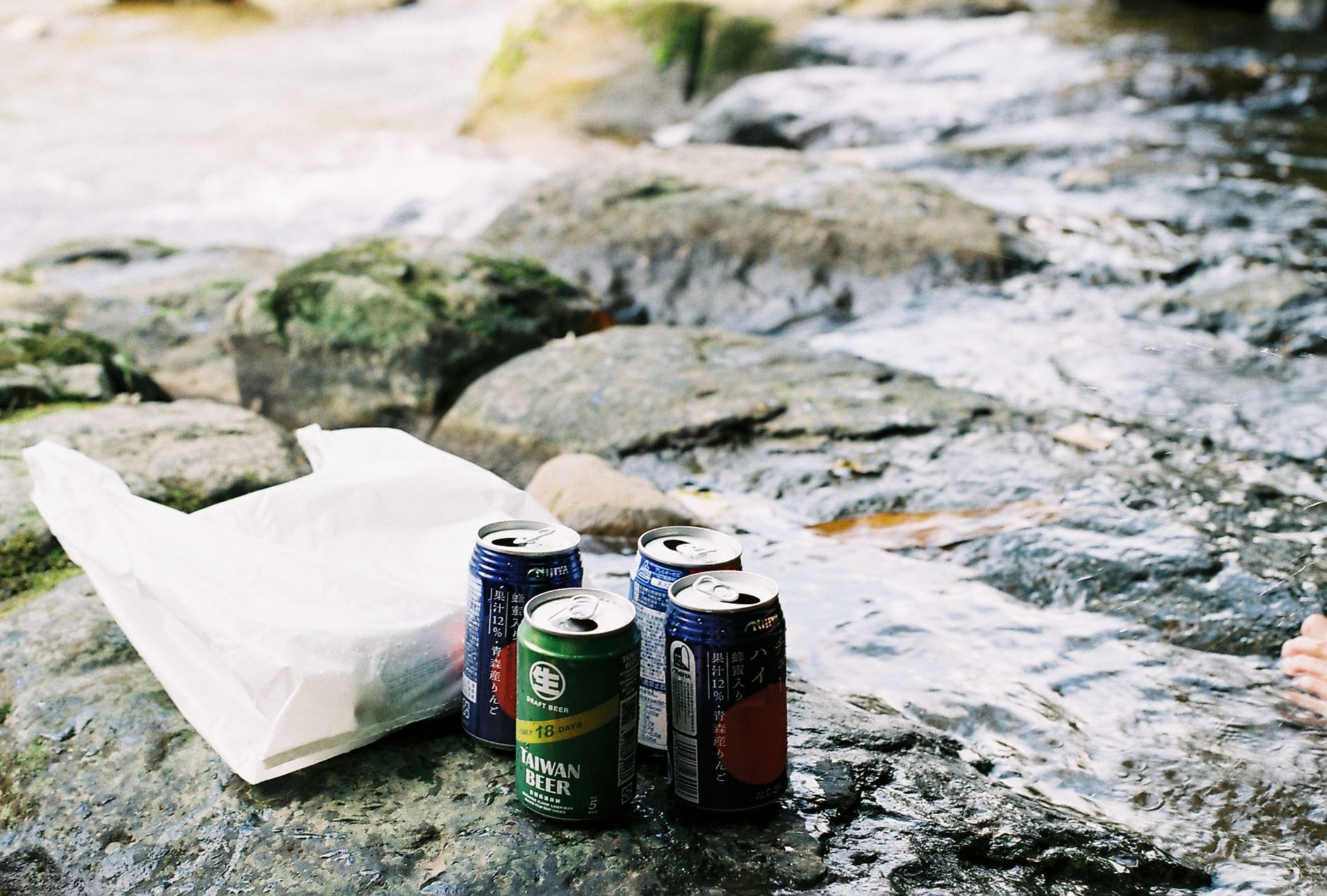 Cans of beer on mossy rocks beside a flowing stream, perfect for outdoor leisure and relaxation.