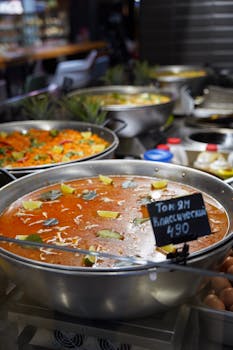 Close-up of traditional Tom Yum soup with ingredients in a restaurant setting, highlighting vibrant flavors.
