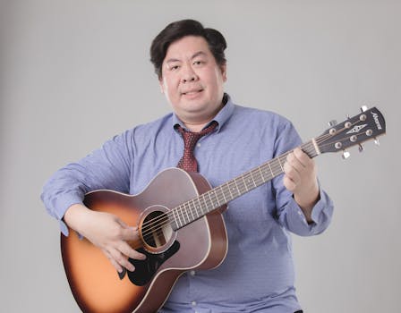 Asian man in a tie playing an acoustic guitar, creating a musical and professional vibe.