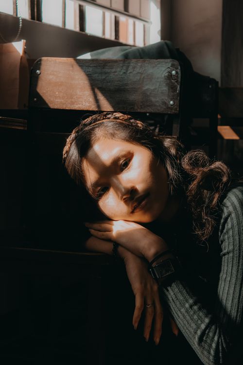 Free Sunlit portrait of a woman leaning on a chair, casting artistic shadows. Stock Photo