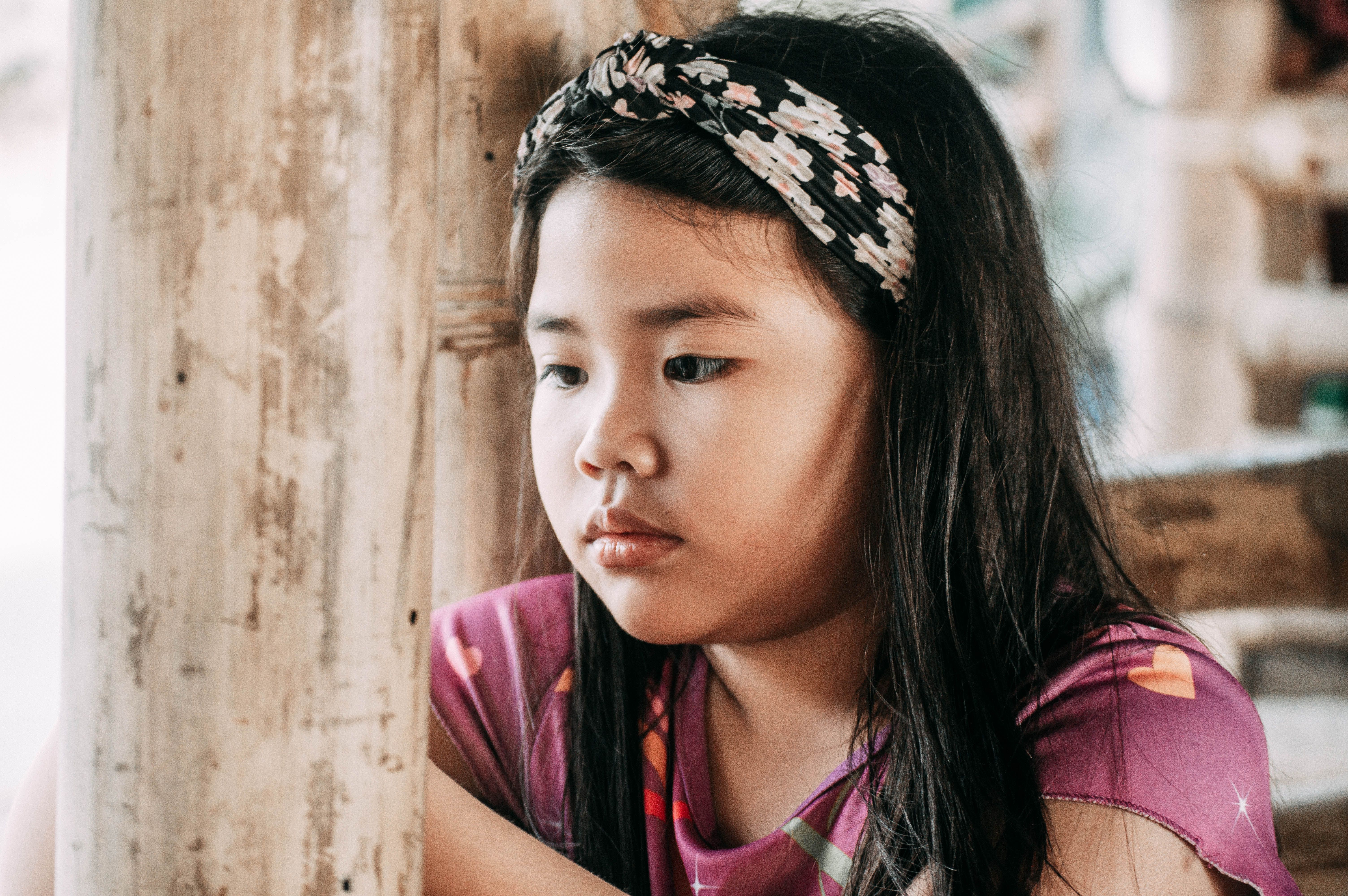 A young girl wearing a floral headband, lost in thought, indoors.