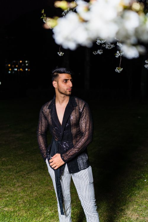 Free Stylish man in a black mesh shirt and striped pants poses outdoors at night under soft lighting. Stock Photo