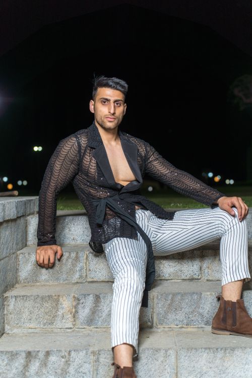 Free A fashionable man poses confidently in black mesh top and striped pants on stone stairs at night. Stock Photo