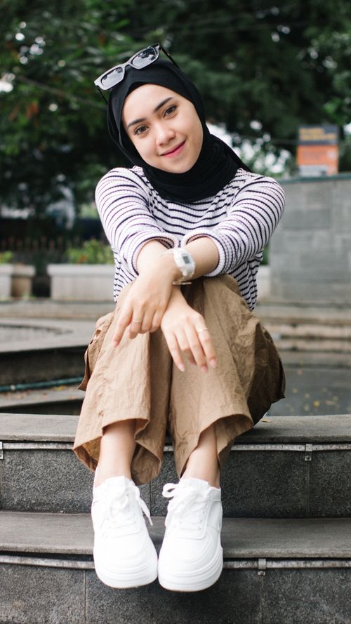 Free Young woman wearing hijab and sunglasses sitting on stairs outdoors, smiling. Stock Photo