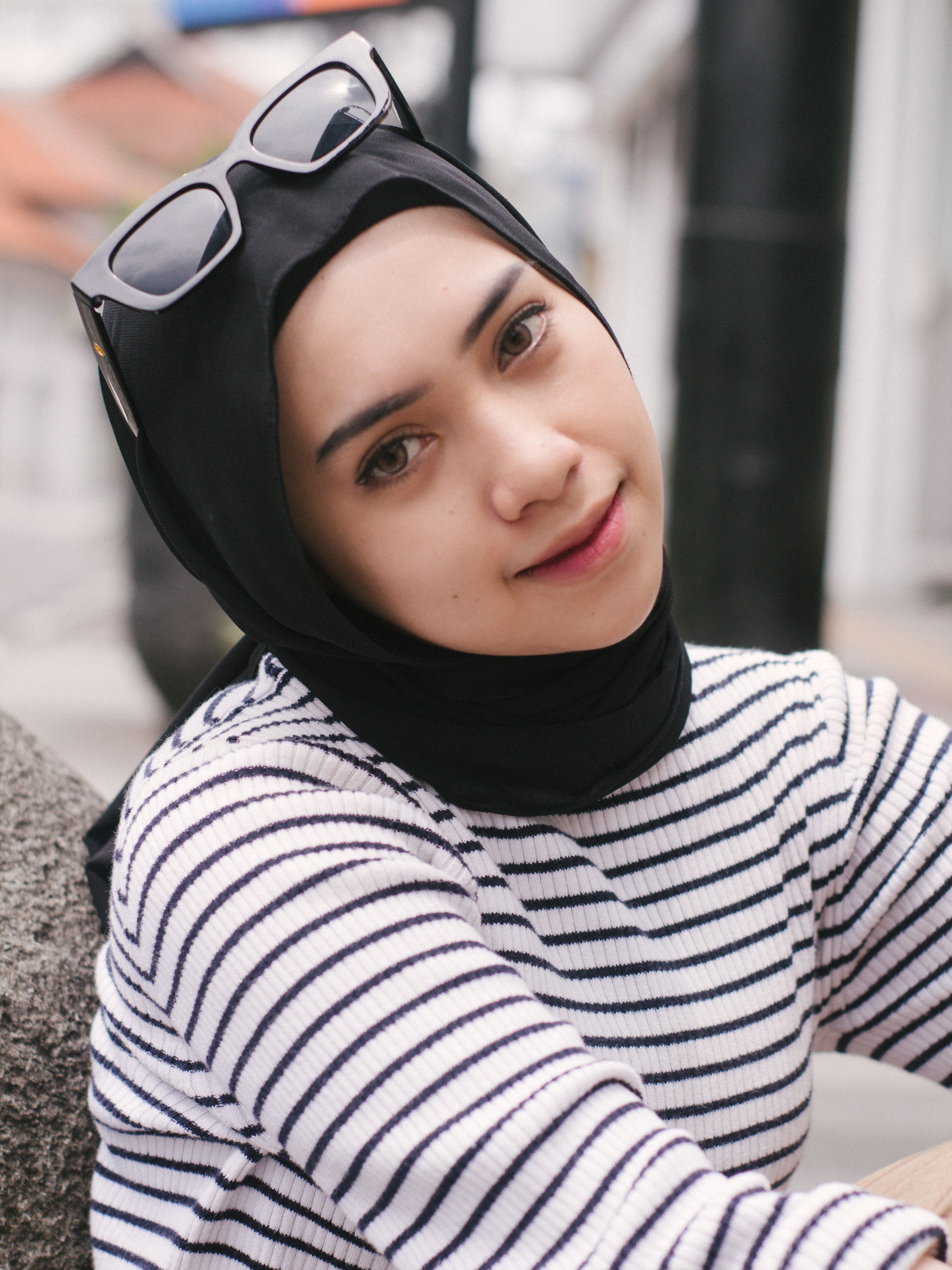 Young woman with headscarf and stripes smiling gently outdoors.