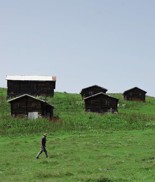 Man Walking on Grass near Wooden Houses in Village