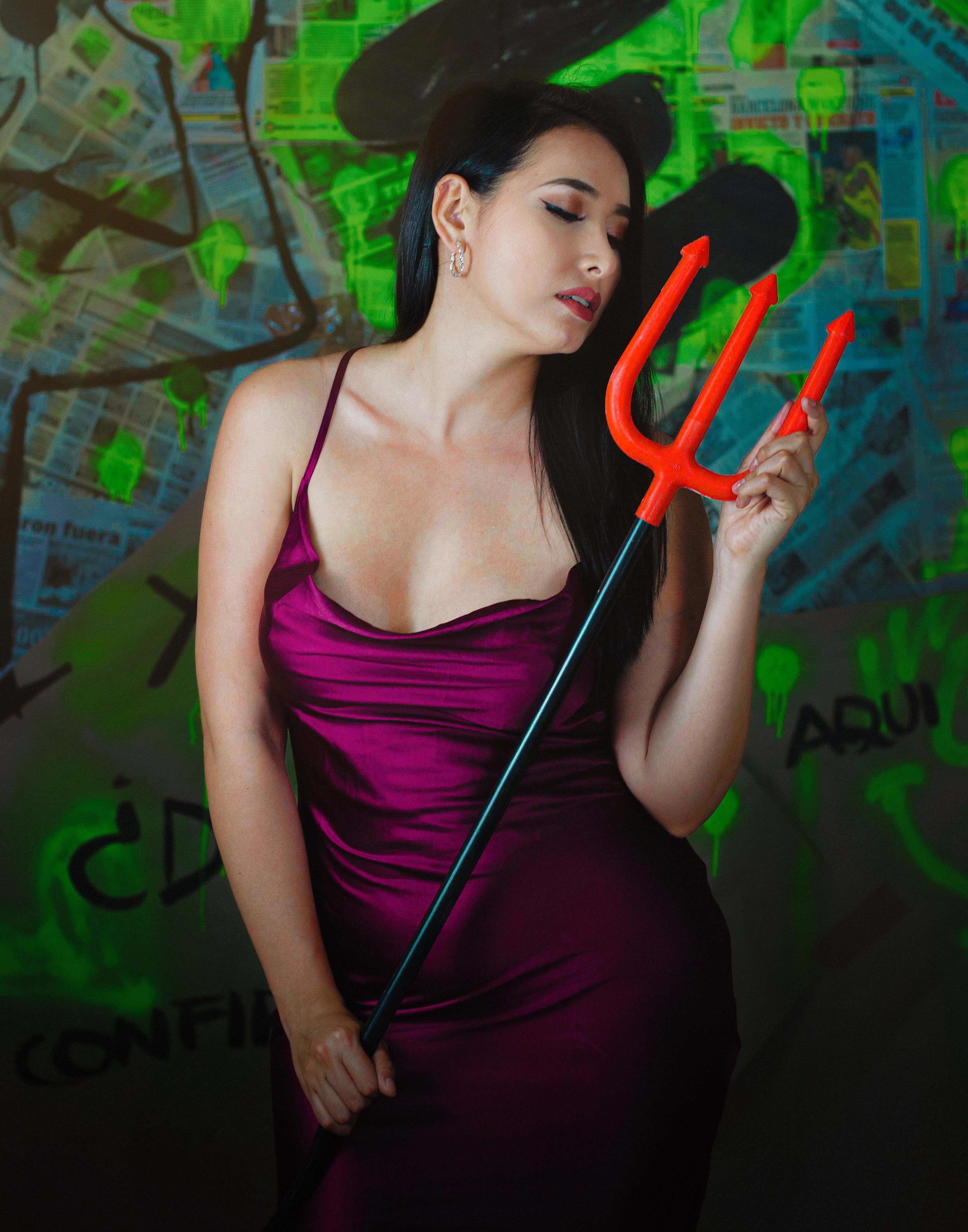 Fashion portrait of a woman in a satin dress, posing with a trident against an artistic background.