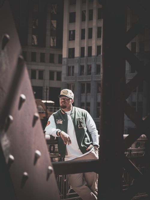 Free Casually dressed man poses confidently against a modern city backdrop, surrounded by buildings. Stock Photo