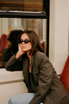 Woman with sunglasses reflecting on a train journey, exuding style and contemplation.