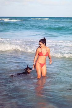 Smiling woman in bikini with dog at the sunlit beach.