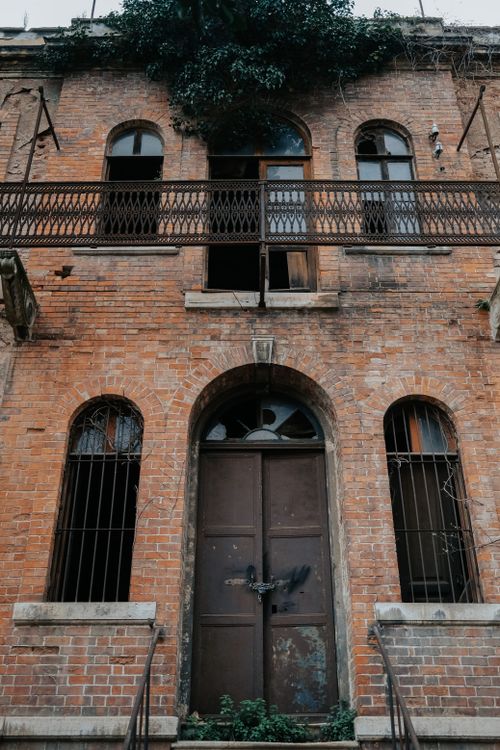 Free A weathered brick facade of an abandoned building with gothic elements and a locked door. Stock Photo