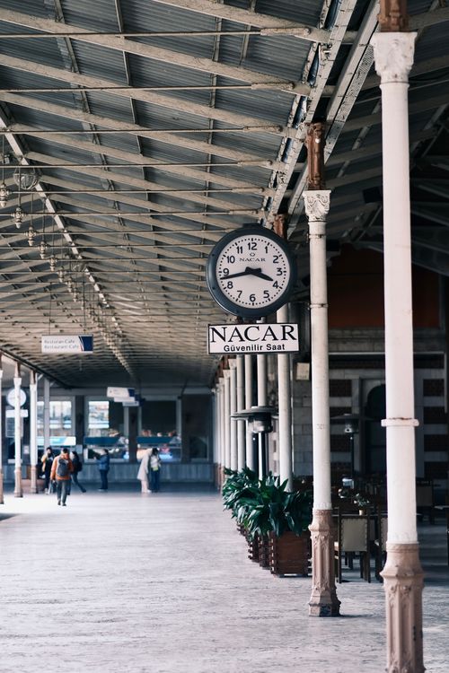 Free A vintage clock and iron columns in a historic railway station setting with travelers. Stock Photo