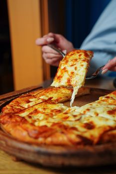 Close-up of a hot cheese pizza slice being lifted from a wooden platter indoors.