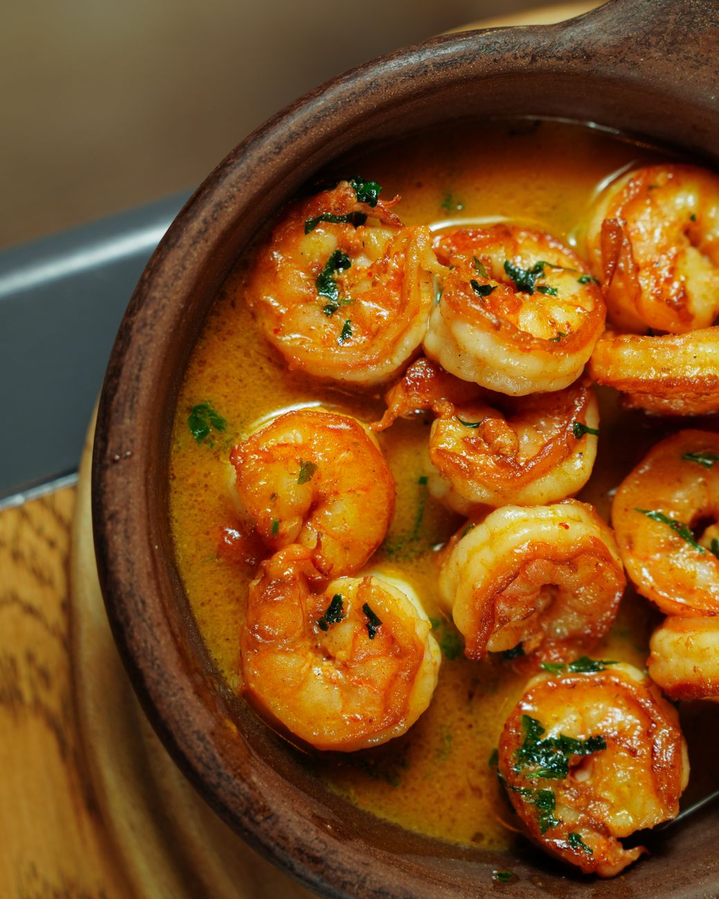 Golden seared shrimp glistening in reddish spiced butter sauce with visible seasonings and bright green parsley garnish in a large skillet