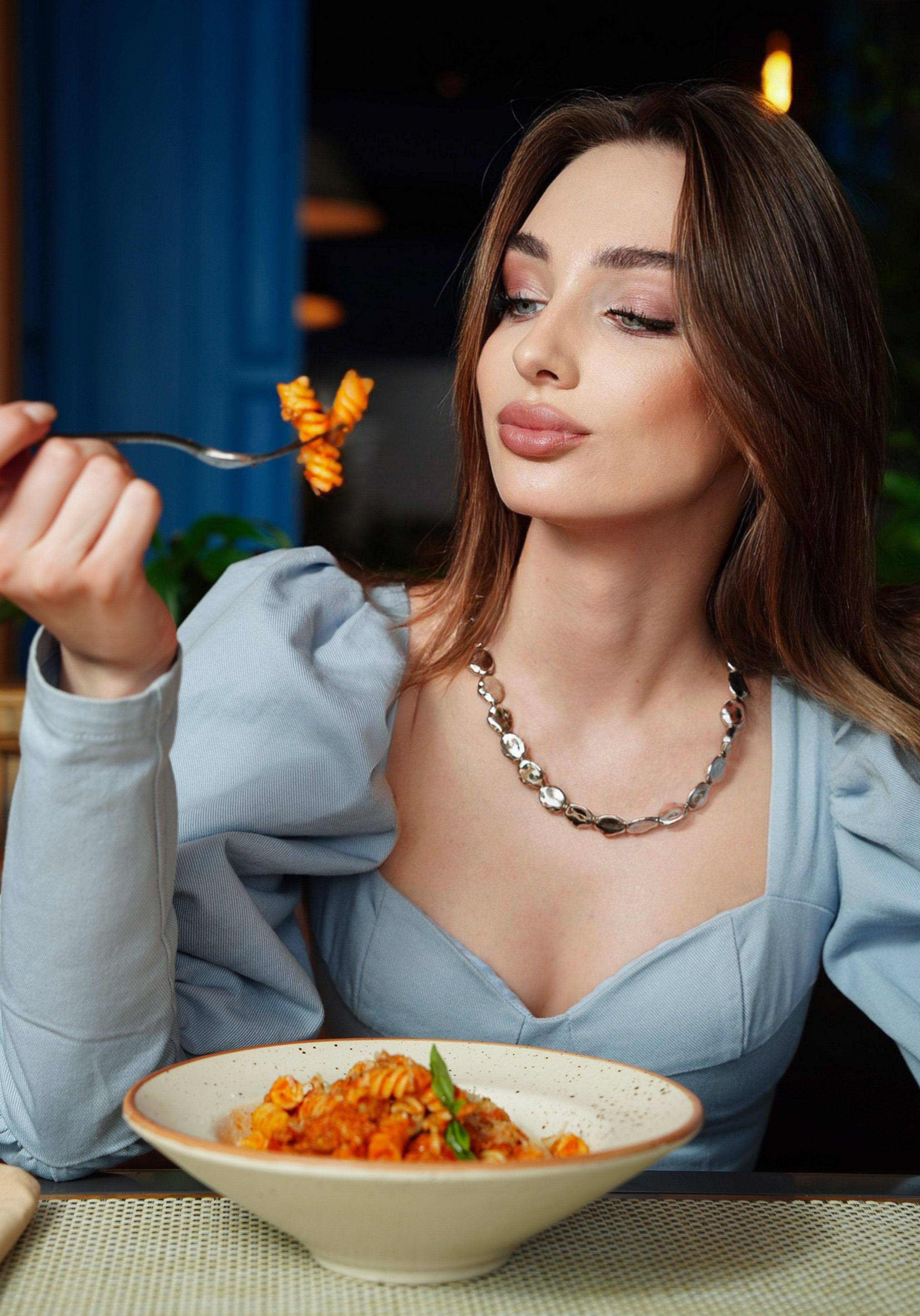 Uma mulher estilosa comendo pasta graciosamente em um restaurante chique, exalando elegância e sofisticação.