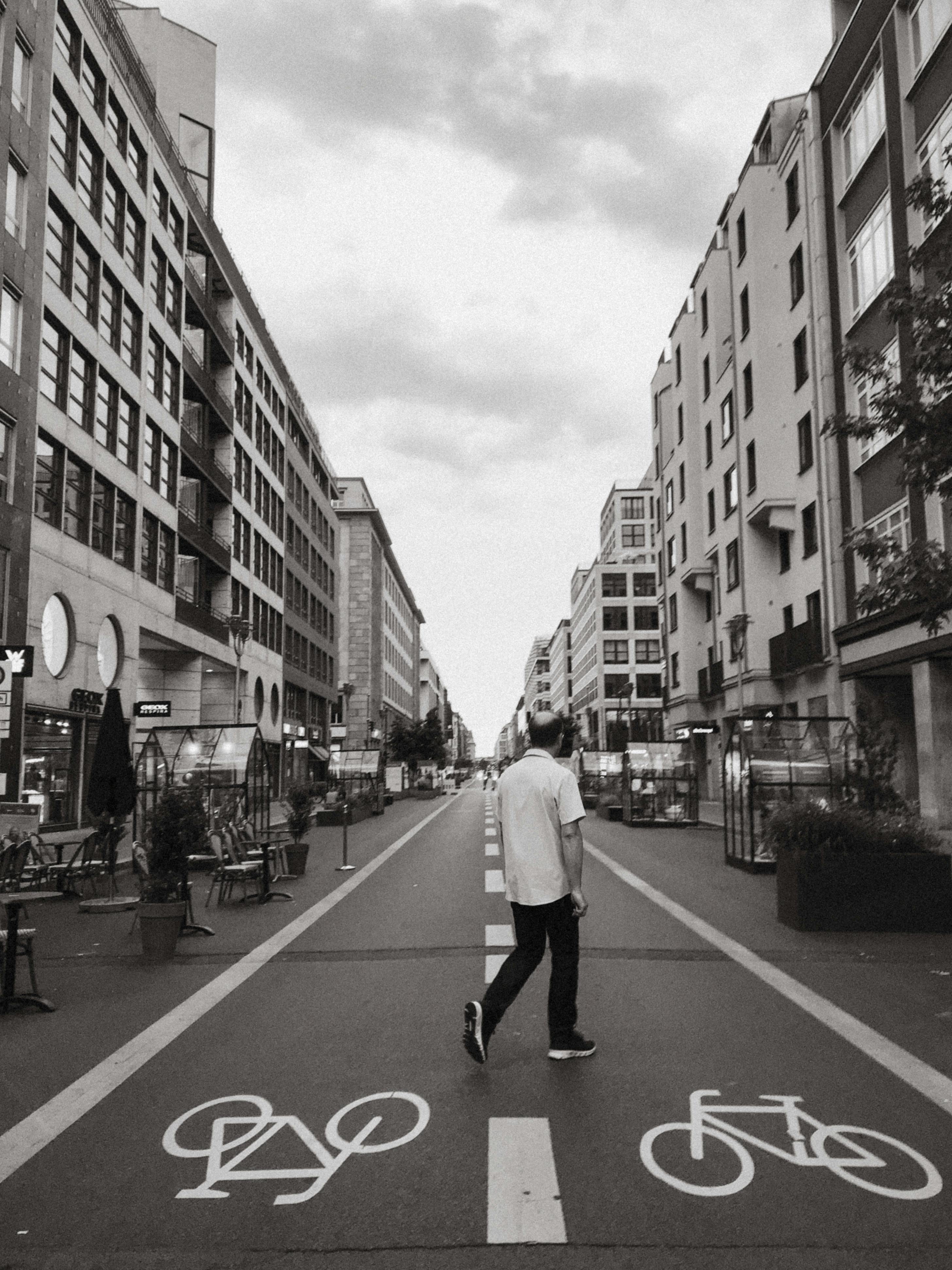 A man walks down a city street in Berlin, featuring bike lanes and surrounding buildings in a black and white setting.