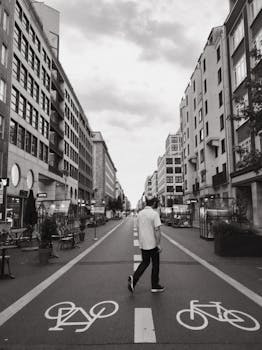 A man walks down a city street in Berlin, featuring bike lanes and surrounding buildings in a black and white setting.