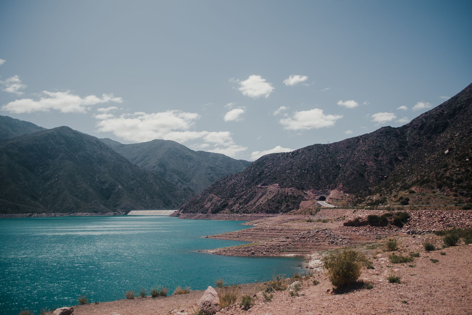 Tranquil turquoise lake surrounded by rocky Andean mountains under a clear summer sky.